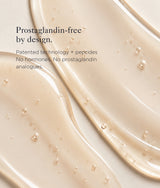 A close-up of a smooth, creamy beige cosmetic serum with small bubbles, overlaid with text reading 'Prostaglandin-free by design. Patented technology + peptides No hormones.